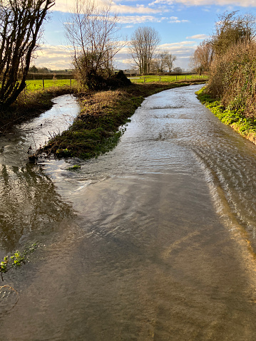 Stream which has burst its banks flooding a rural lane after Storm Henk, Somerset, England