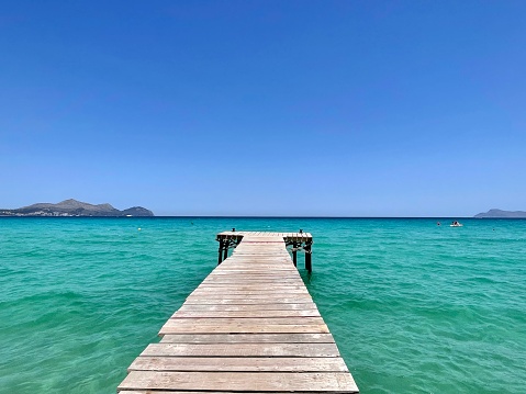 View of the horizon in the Mediterranean Sea. Wooden bridge, blue and light turquoise water. Mallorca, Balearic Islands. Sunny day and clear sky.