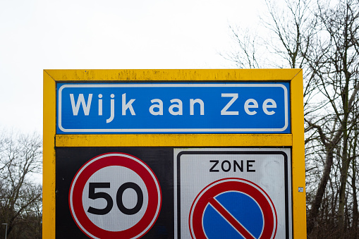 Location sign of the coastal village of Wijk aan Zee, Netherlands. Below are signs of a speed limit of 50 and a no parking sign.