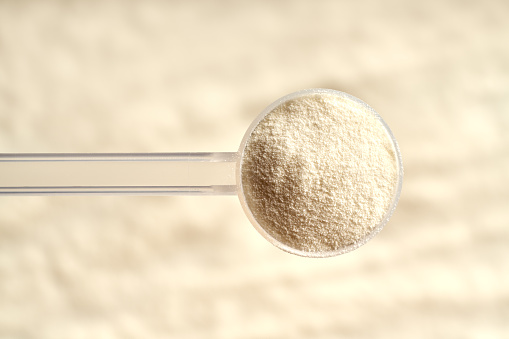 Collagen powder in a plastic measuring spoon above beige background, top view