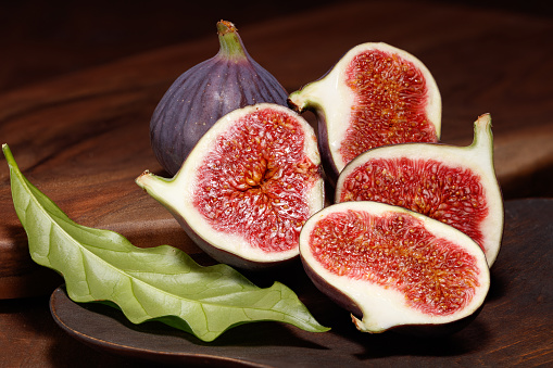 Cutting few figs on a wooden background. Ripe delicious fresh figs. Whole, sliced figs and leaf on a cutting board. Selective focus