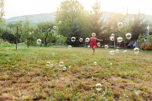 Little girl having fun catching soap bubbles in the yard