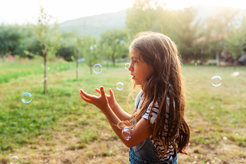Little girl having fun catching soap bubbles in the yard