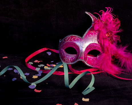 Venetian carnival pink mask with black background and confetti