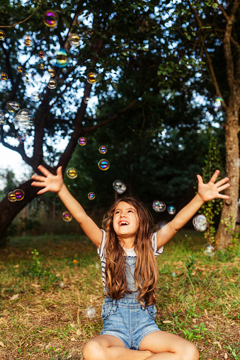 Little girl having fun catching soap bubbles in the yard