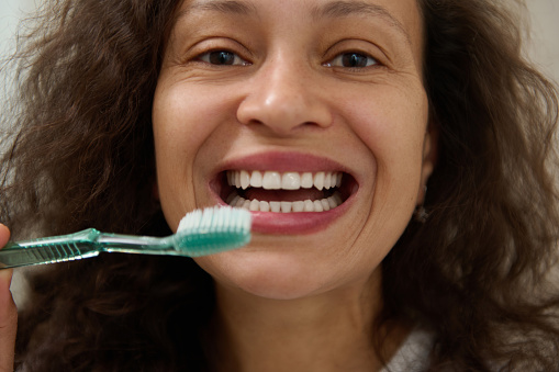 Happy multi ethnic woman smiling with beautiful toothy smile, holding a toothbrush near her face and confidently looking at the camera. The concept of healthy lifestyle, oral care and dental hygiene