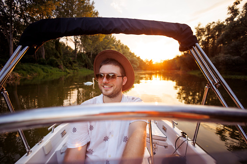 Handsome young man having fun and relaxing riding a boat in sunset while on summer vacation