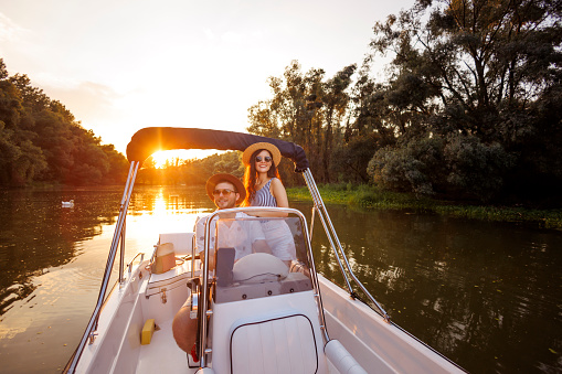 Beauitful young couple in love having fun and relaxing riding a boat to the sunset while on summer vacation or weekend getaway from the city