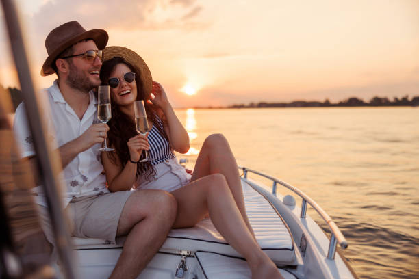 Couple hugging and drinking champagne while sailing to the sunset on a boat stock photo