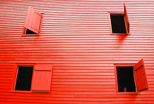 Solid red shutters on a bright red, two-story, New England barn opened at various angles. Shiplap construction.