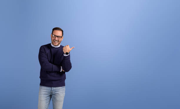 portret szczęśliwego przedsiębiorcy celującego kciukiem w miejsce na kopię do marketingu na odizolowanym niebieskim tle - celowanie zdjęcia i obrazy z banku zdjęć