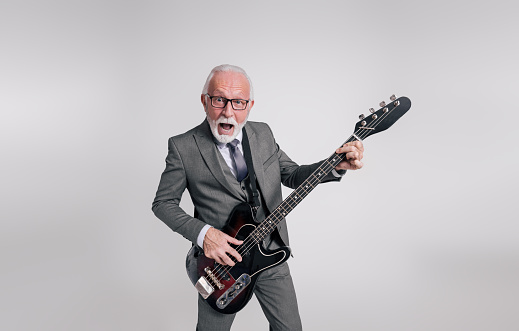 Senior businessman with mouth open singing ecstatically and playing guitar over white background