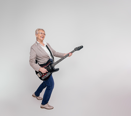 Full length of cheerful senior businesswoman singing and playing electric guitar on white background