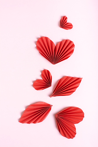 Beautiful composition of folded red paper hearts and leaves on a pink background  vertical view