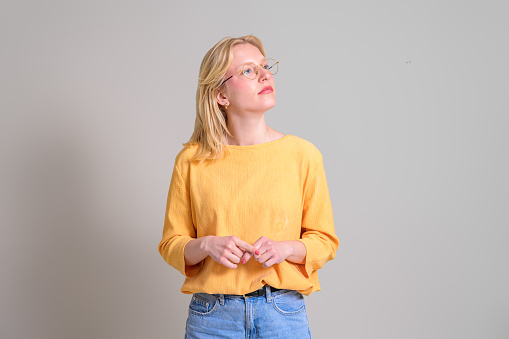 Thoughtful female entrepreneur with blond hair and eyeglasses looking away over white background