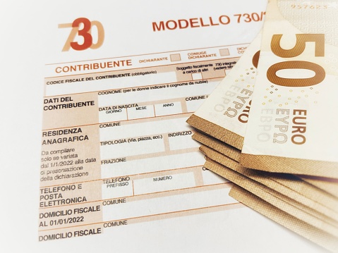 Province of Florence , January 14th 2024, many euro banknotes with the Modello 730 as background , translating in Italian as declaration of incomes , concept of tax payment .