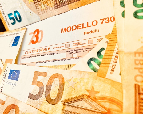 Province of Florence , January 14th 2024, many euro banknotes with the Modello 730 as background , translating in Italian as declaration of incomes , concept of tax payment .
