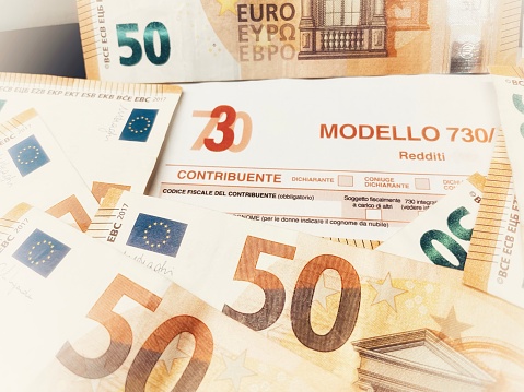 Province of Florence , January 14th 2024, many euro banknotes with the Modello 730 as background , translating in Italian as declaration of incomes , concept of tax payment .