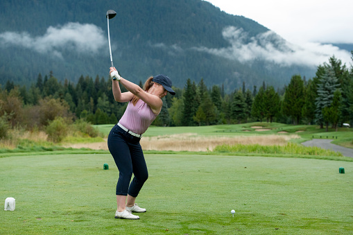 Woman golfs in mountain environment on moody day