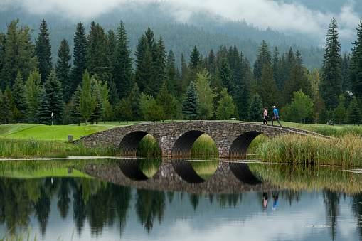 Couple walk across bridge on mountain golf course on moody day