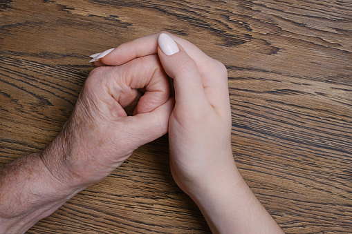 The hand of a young woman carefully supports the wrinkled hand of an old woman. Family and Care, World Day for Grandparents and the Elderly concept. Helping hand. Caring for the health of the elderly.