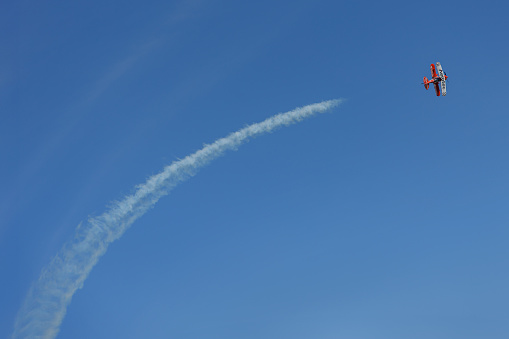 Mar del Plata, Argentina - January 14th, 2023: Biplane airplane doing stunts in the sky and releasing smoke.