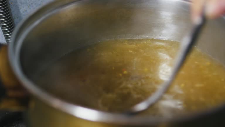 Stirring boiling fatty golden rich flavorful meat beef pork broth with a spoon.