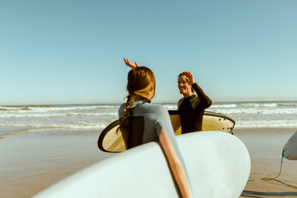 istock Surfer meets friend by waving hand while carrying surfboard on the beach 1933345784