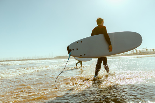 Male surfer in wetsuit with his surfboard entering the sea. Surfing on ocean. High quality photo
