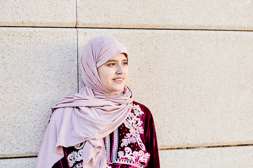 Portrait of a beautiful muslim girl wearing hijab looking at the camera. In the background a wall outside. Space for copy.