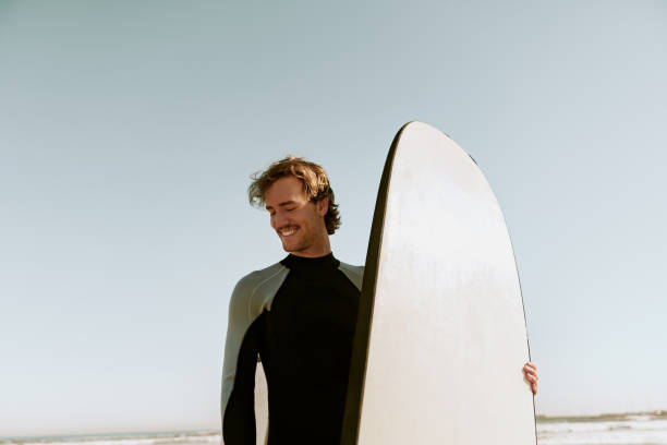 istock Male surfer in wetsuits standing with surfboard and preparing for ride on waves 1933358385