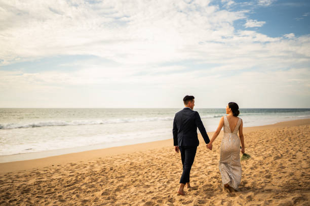 istock Bride and groom walking through the beach 1933359449