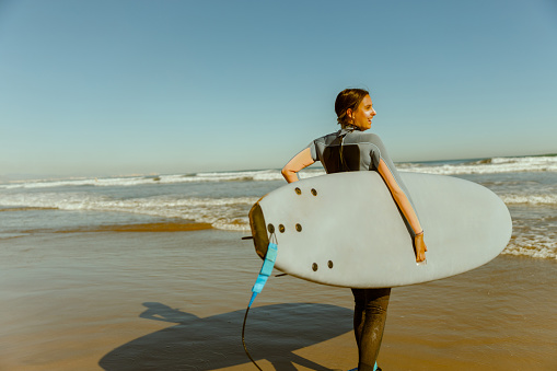 Female surfer in wetsuit with his surfboard entering the sea. Surfing and ocean. High quality photo