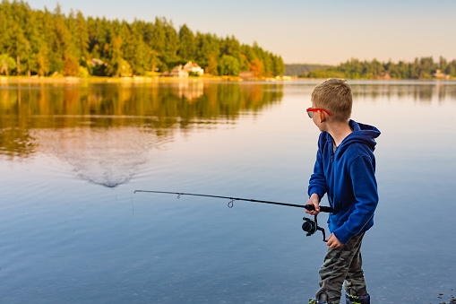 a boy is fishing on the lake and looking at the camera