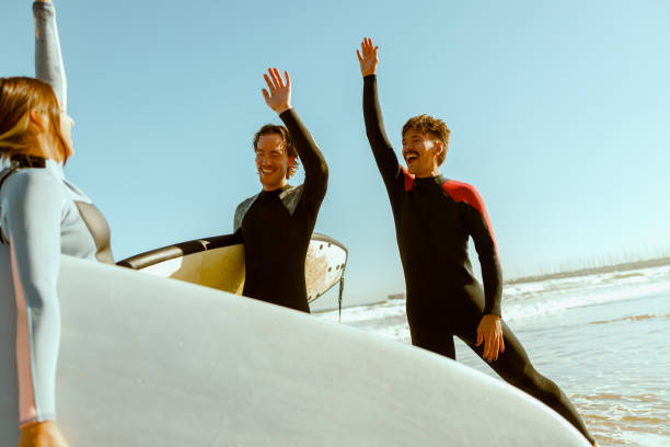 istock Surfers meets friends by waving hand while carrying surfboard on the beach 1933361622