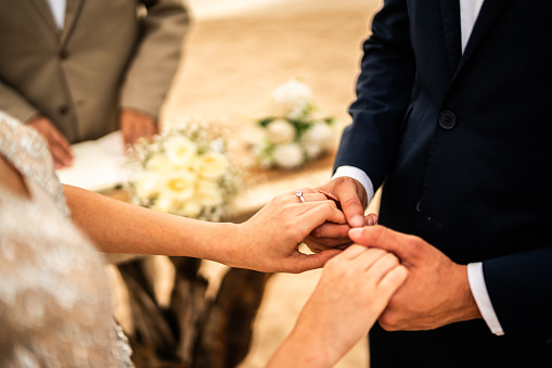 Close-up of a bride and groom holding hands in wedding ceremony on  the beach