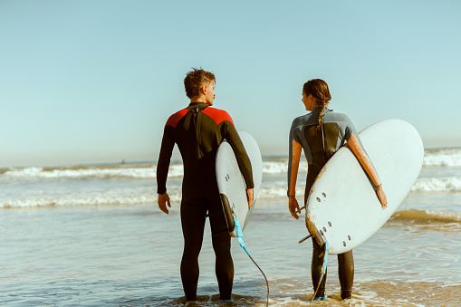 Couple of surfers with surfboards standing on the beach and looking each other. High quality photo