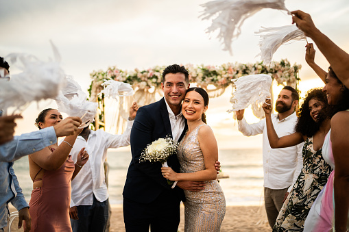 Portrait of newlyweds celebrating with their guests at beach wedding ceremony