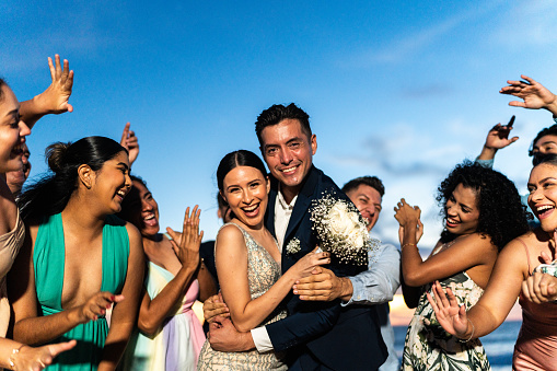 Portrait of bride and groom celebrating with their friends on beach wedding party