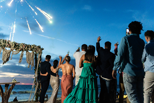 Bride and groom watching fireworks with wedding guests on the beach