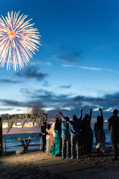 Bride and groom watching fireworks with wedding guests on the beach