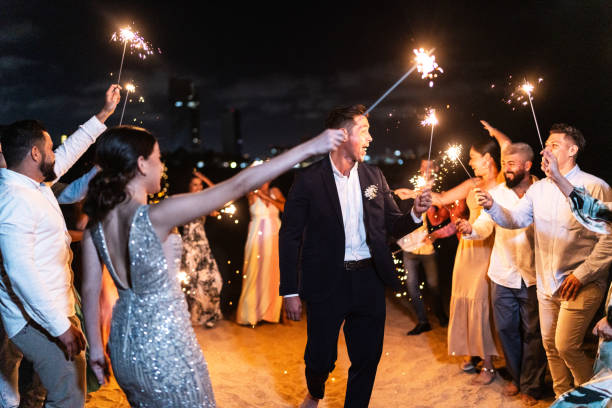 istock Bride and groom using sparklers with their wedding guests on the beach wedding party 1933378873