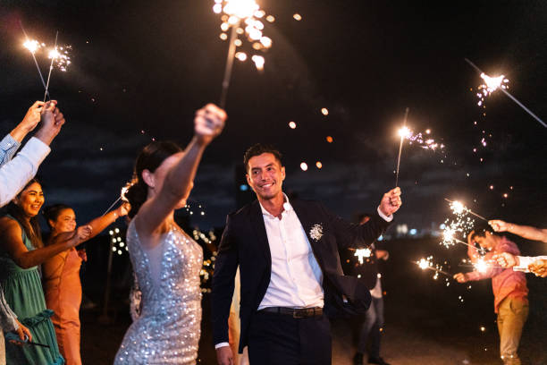 istock Bride and groom using sparklers with their wedding guests on the beach wedding party 1933378875