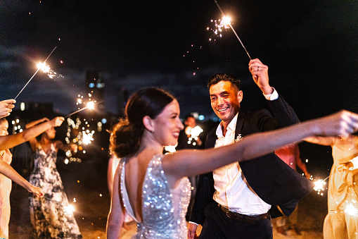 Bride and groom using sparklers with their wedding guests on the beach wedding party