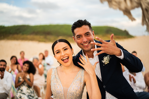 Portrait of a bride and groom showing their wedding rings in wedding ceremony on the beach