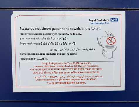 Reading, UK - October 22, 2023: A multilingual NHS poster in an NHS hospital public lavatory instructing people not to throw paper towels into the toilet.