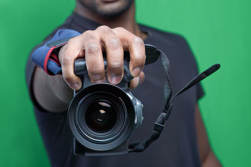 African photographer with DSLR camera, capturing moments on green screen. Close-up of hands holding professional equipment.