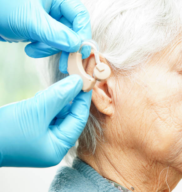 istock Doctor install hearing aid on senior patient ear to reduce hearing loss problem. 1933482020