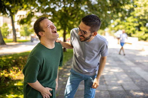 Man with down syndrome having a laugh with his male friend in park.