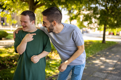 Man with down syndrome having a laugh with his male friend in park.